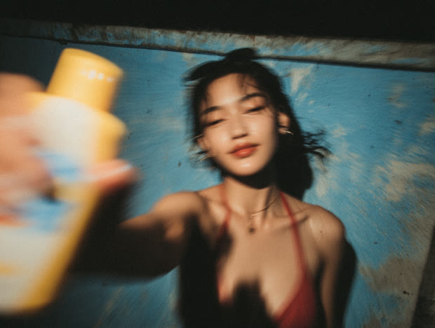 Sunscreen bottle held out toward the camera by a poolside wall