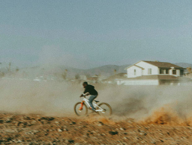 Cyclist riding through dust past a lone house