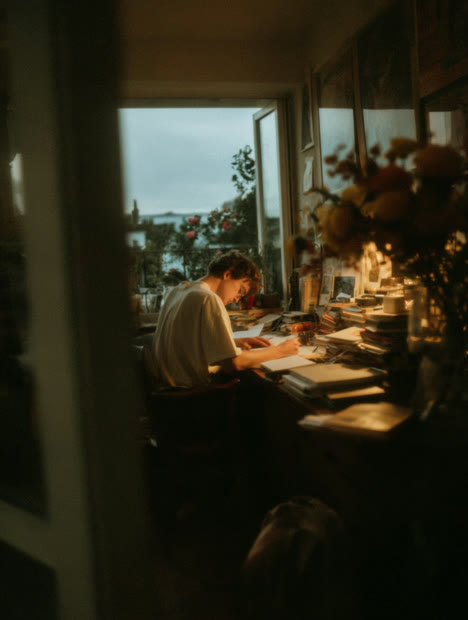 Person writing at a desk seen through a doorway