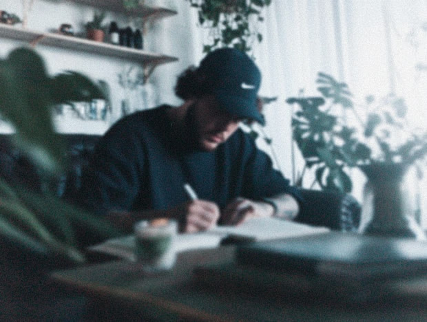 Man in a cap writing at a plant-filled desk