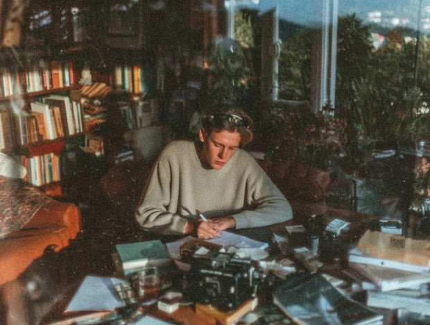 Writer at a desk in a room crowded with books